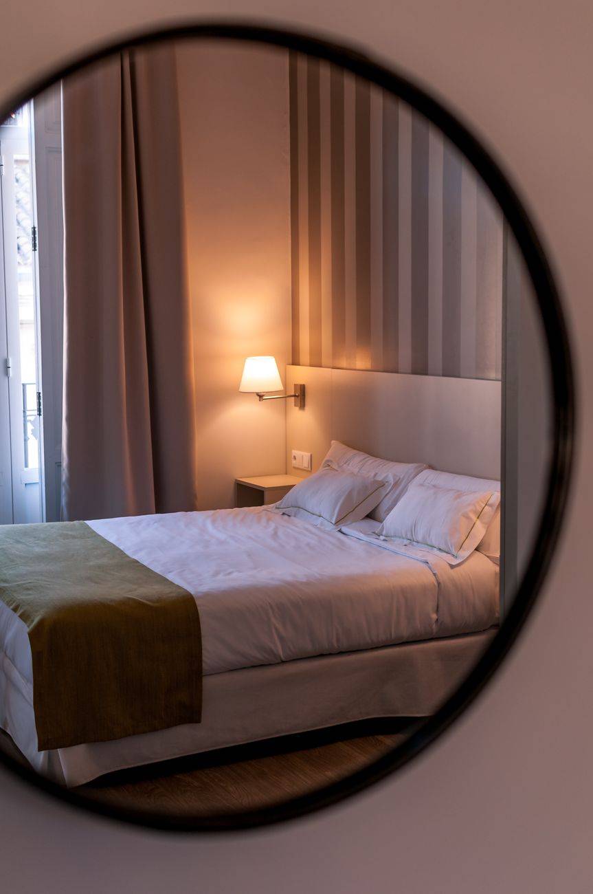 Elegant and cozy hotel bedroom with warm lighting reflected in a mirror.