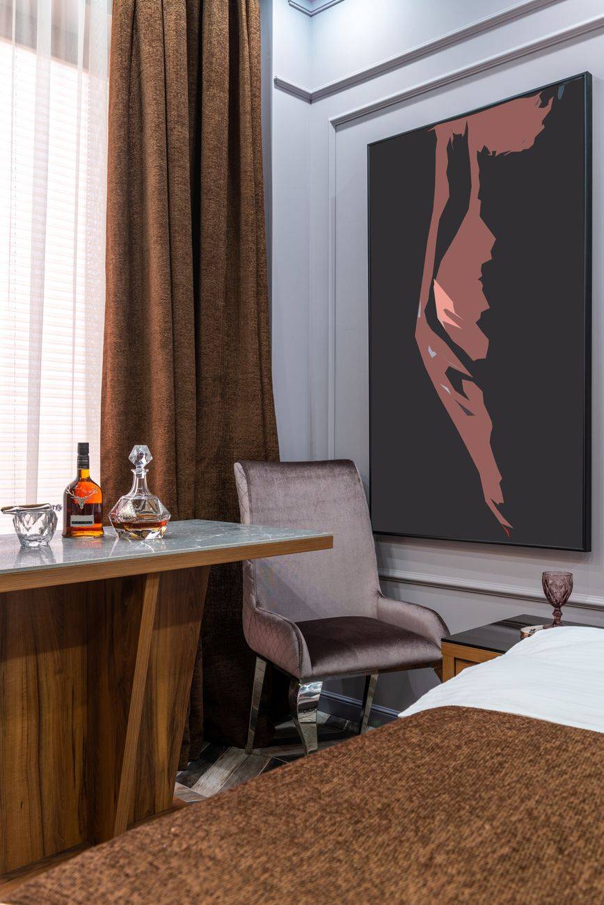 Modern hotel room interior with bed against carafe and bottle of alcoholic beverage on table