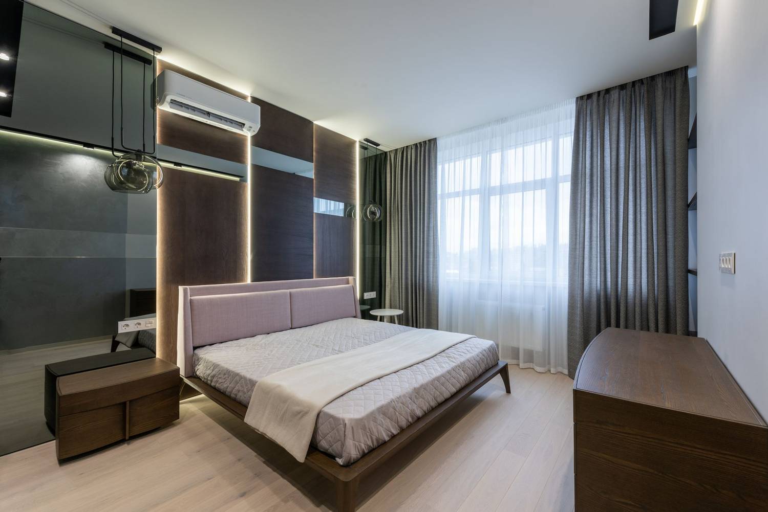 Comfortable bed with wooden nightstand and chest of drawers in modern bedroom decorated with curtains and lamps