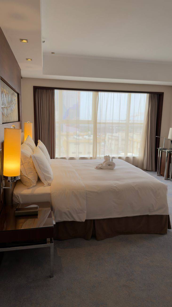 Elegant hotel room with modern decor, large bed, and sunlit window view.