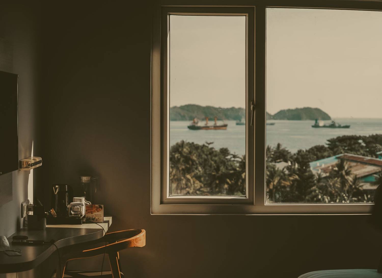 Calm Indonesian sea view from a cozy room window with ships in the distance.