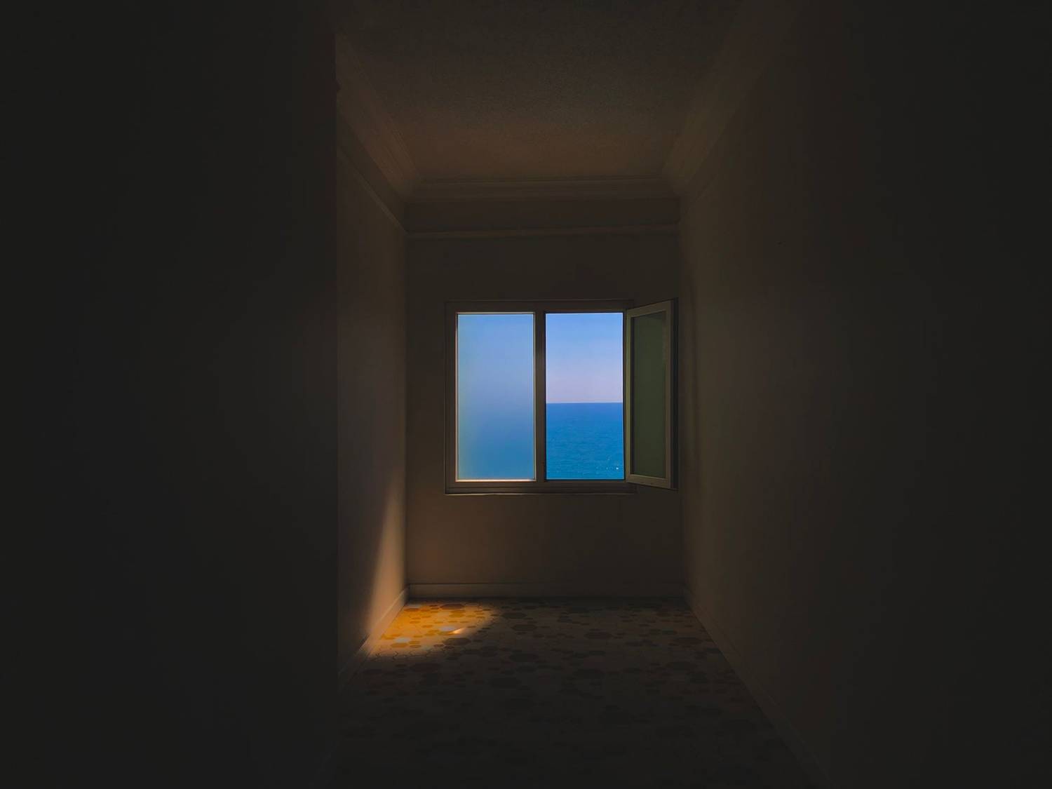 Dark room with an open window showcasing a blue sea horizon.