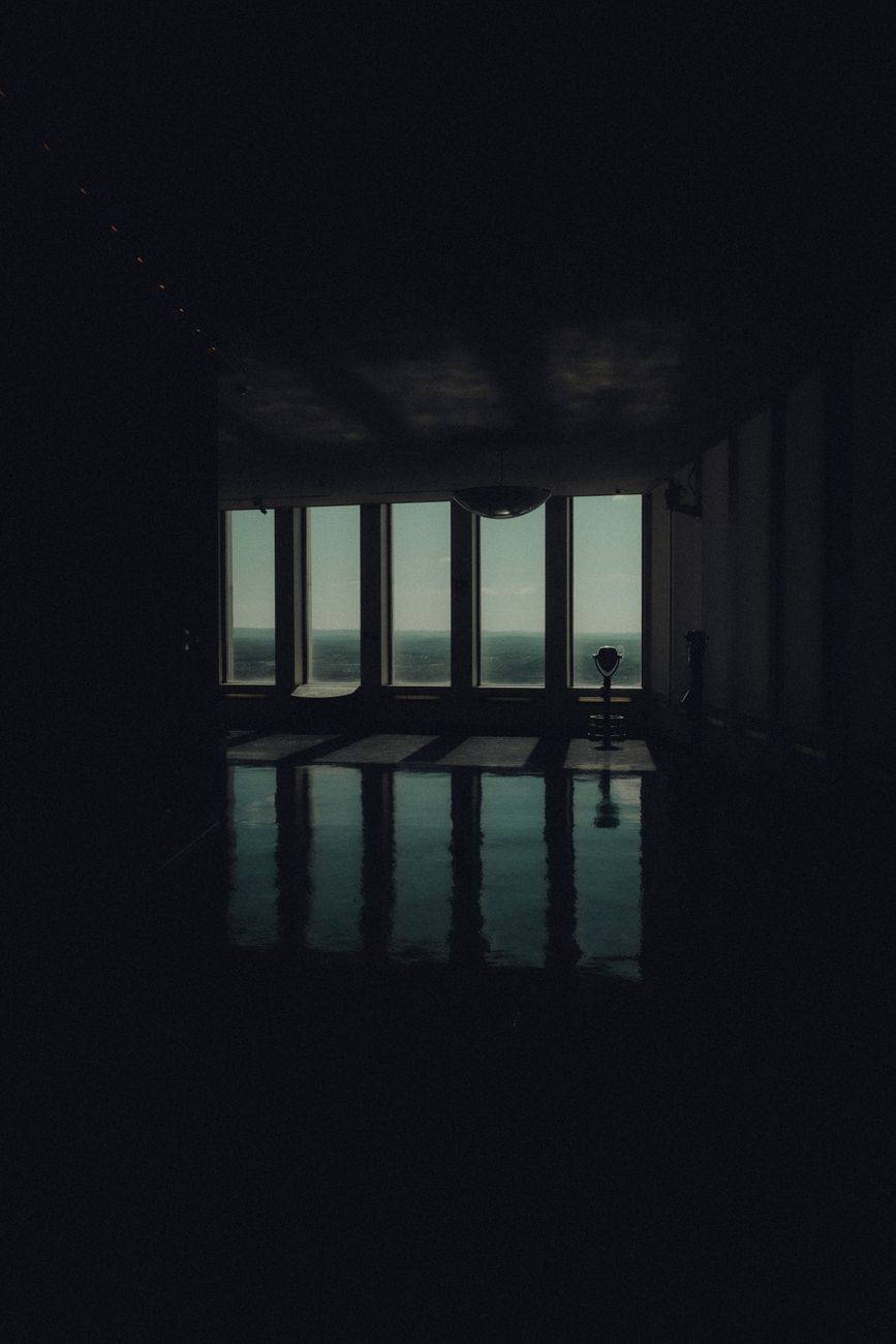 Dramatic shot of a dark interior room with ocean view through large windows casting reflections.