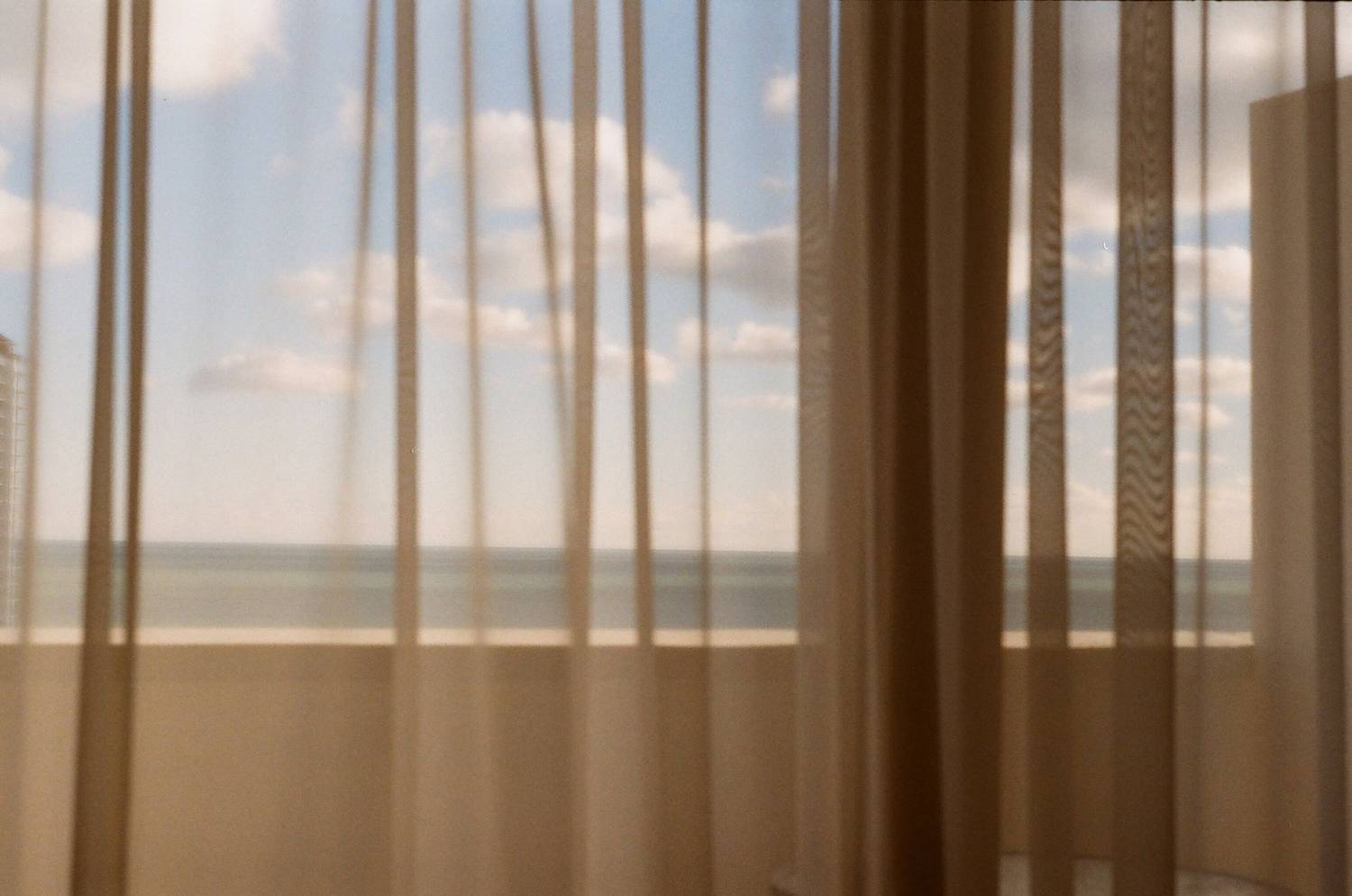 Calm ocean view through sheer curtains, blending indoor warmth with outdoor serenity.