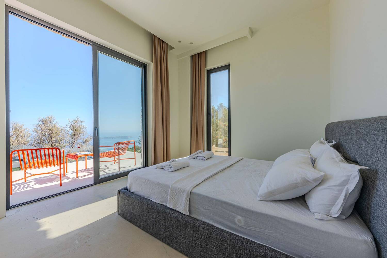 Bright minimalist bedroom featuring a bed, large windows, and ocean view.