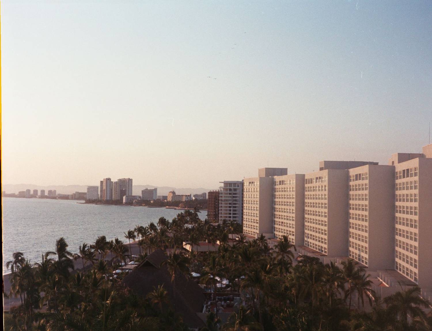 Sunlit beachfront cityscape showcasing tall hotels along the coastline under a clear sky.