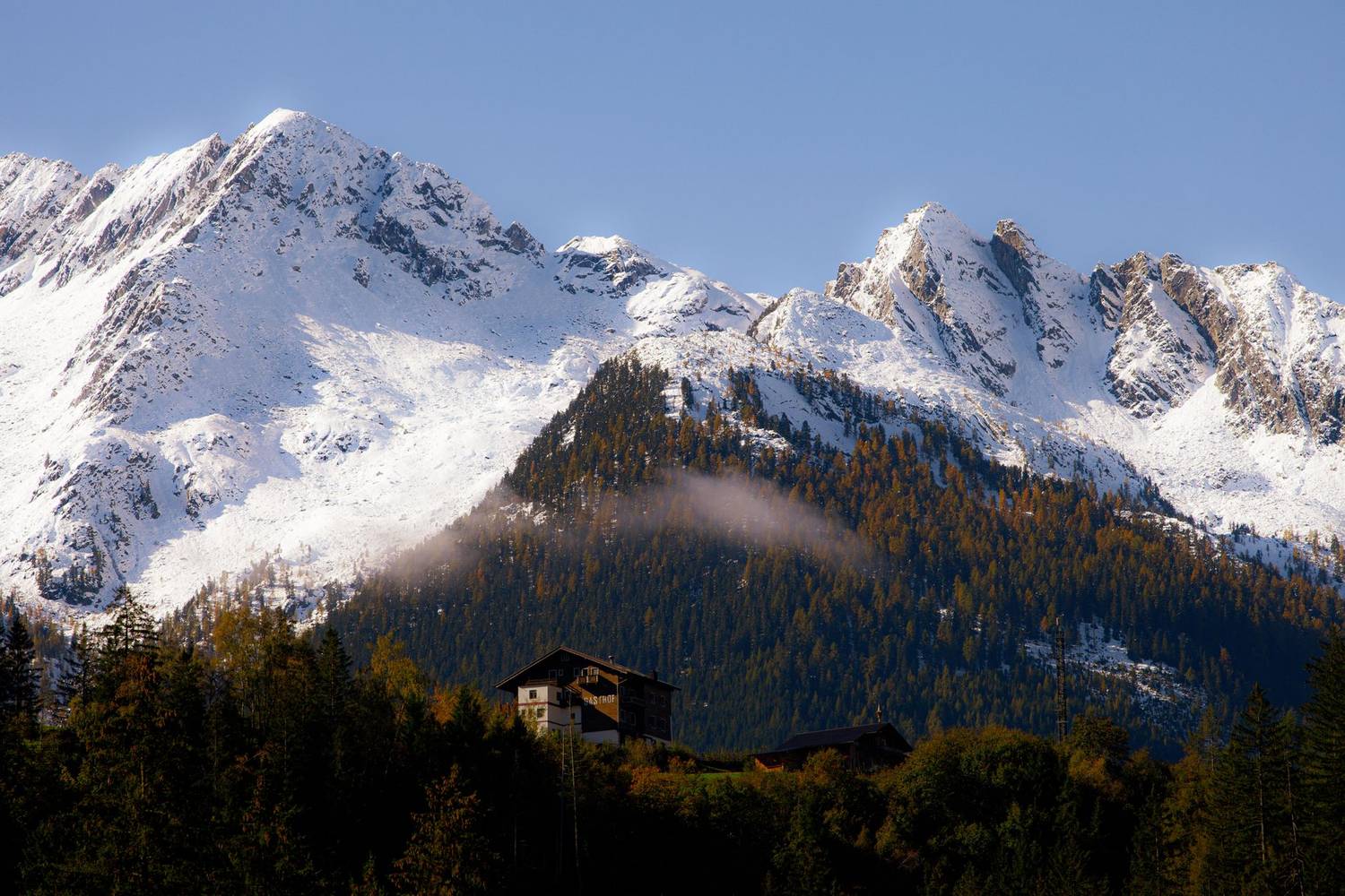 Stunning view of Alpine mountains with snow and autumn forest.