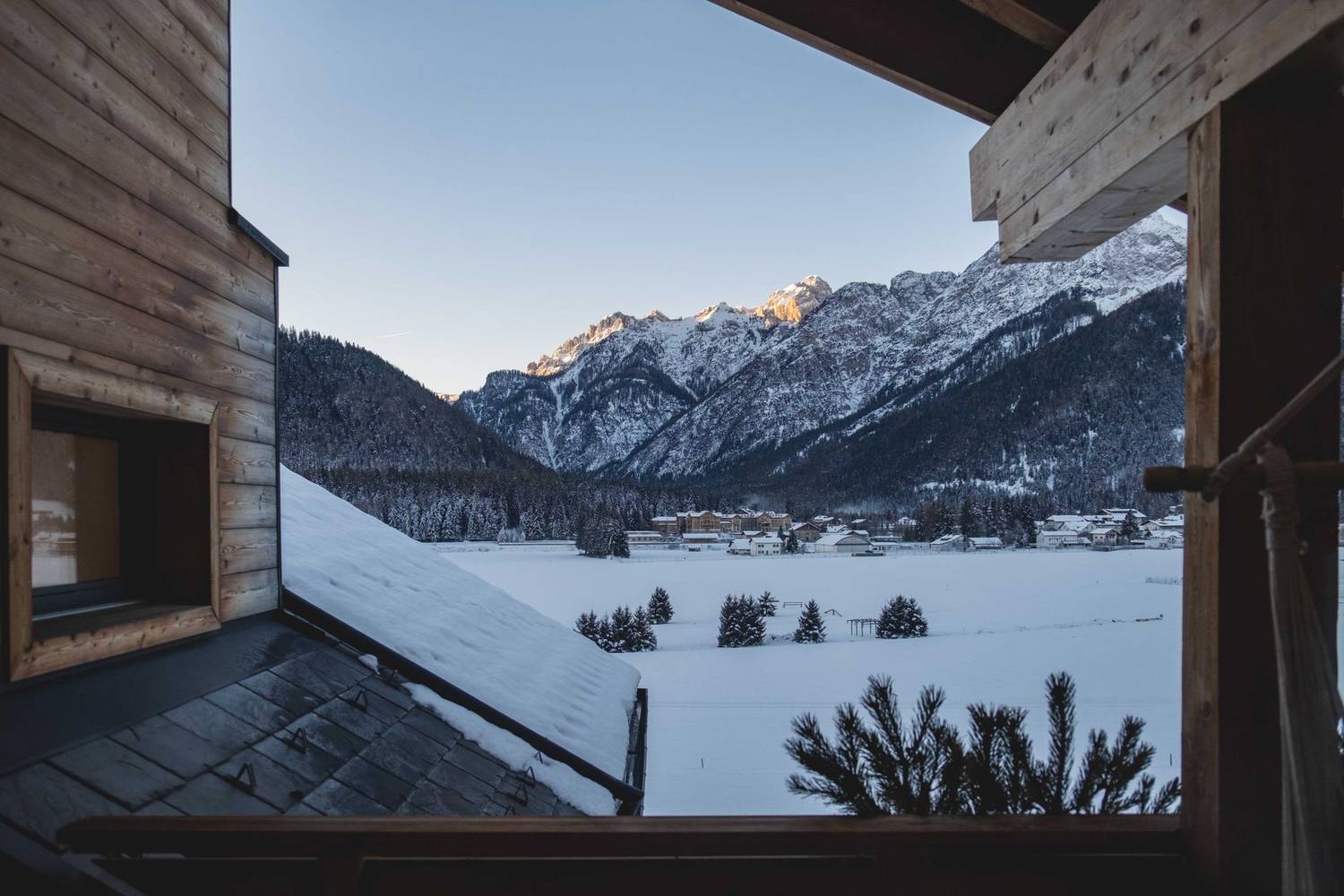 A serene winter scene with a wooden cabin, snow-covered landscape, and majestic mountains.
