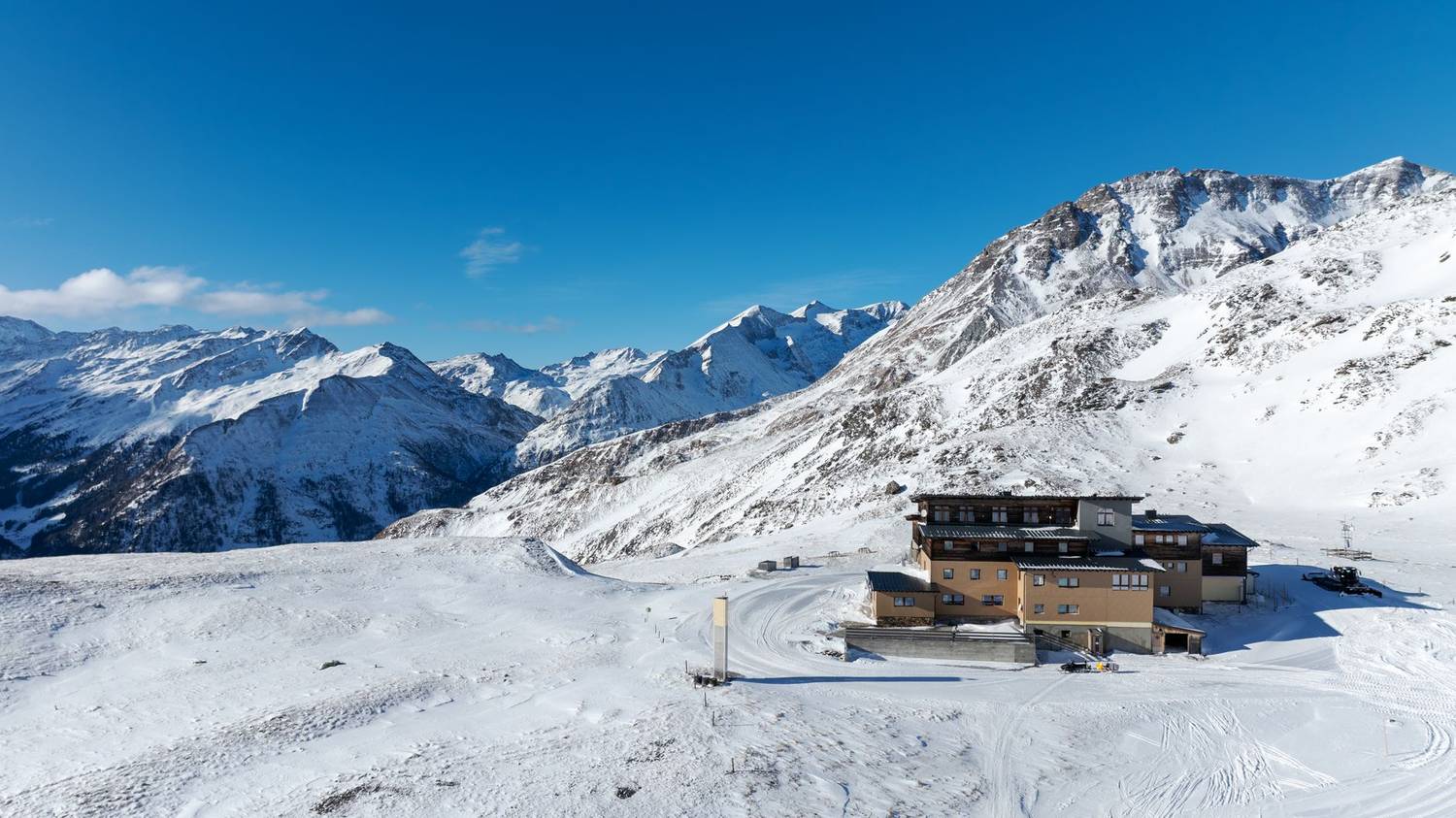 Scenic view of a snowy mountain cabin and peaks in Korutany, Rakousko under a clear blue sky.