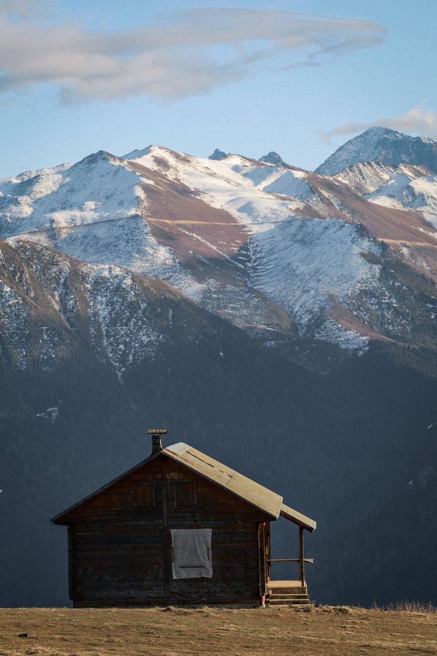 A wooden cabin sits peacefully on a snowy plateau with majestic mountainous backdrop in Rize.