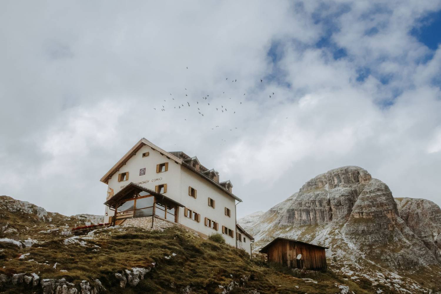 A picturesque mountain lodge sits beneath cloudy skies in an alpine region, offering a serene retreat.