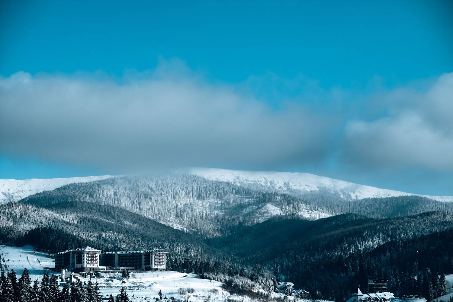 Scenic winter landscape with a hotel resort nestled in snow-covered mountains under a clear blue sky.