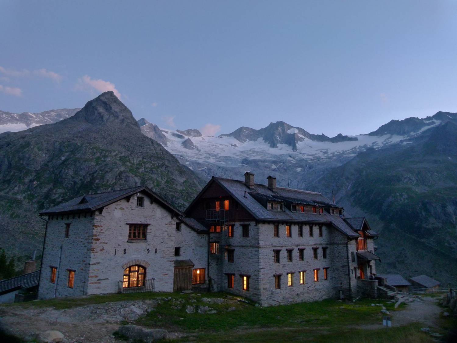 Charming stone lodge with glowing windows set in a rugged alpine landscape at dusk.