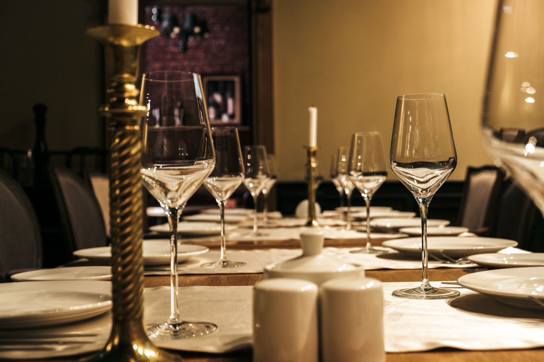 An intimate dining table set with wine glasses and brass candlesticks under warm low light