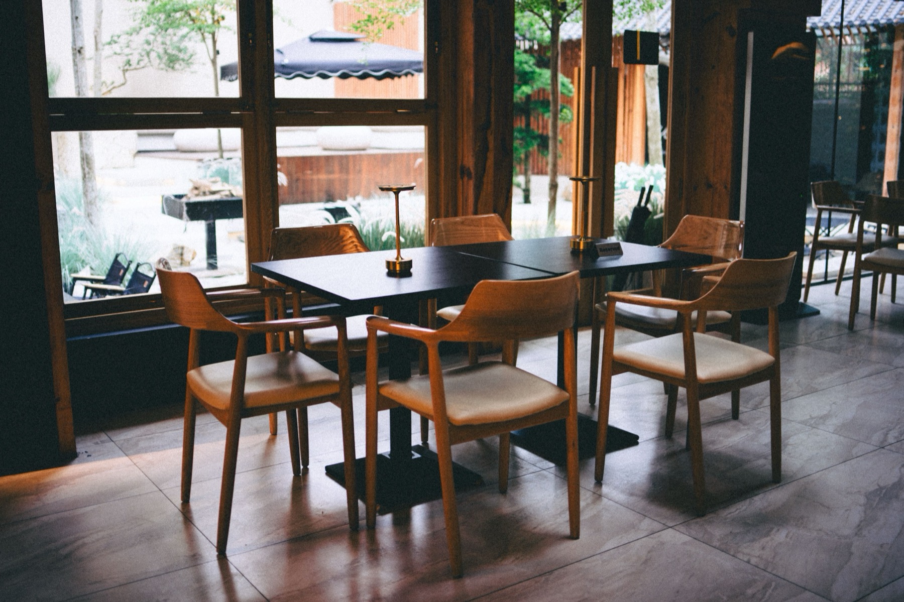Minimal Nordic restaurant with pale wood chairs, dark tables and floor-to-ceiling windows onto a garden