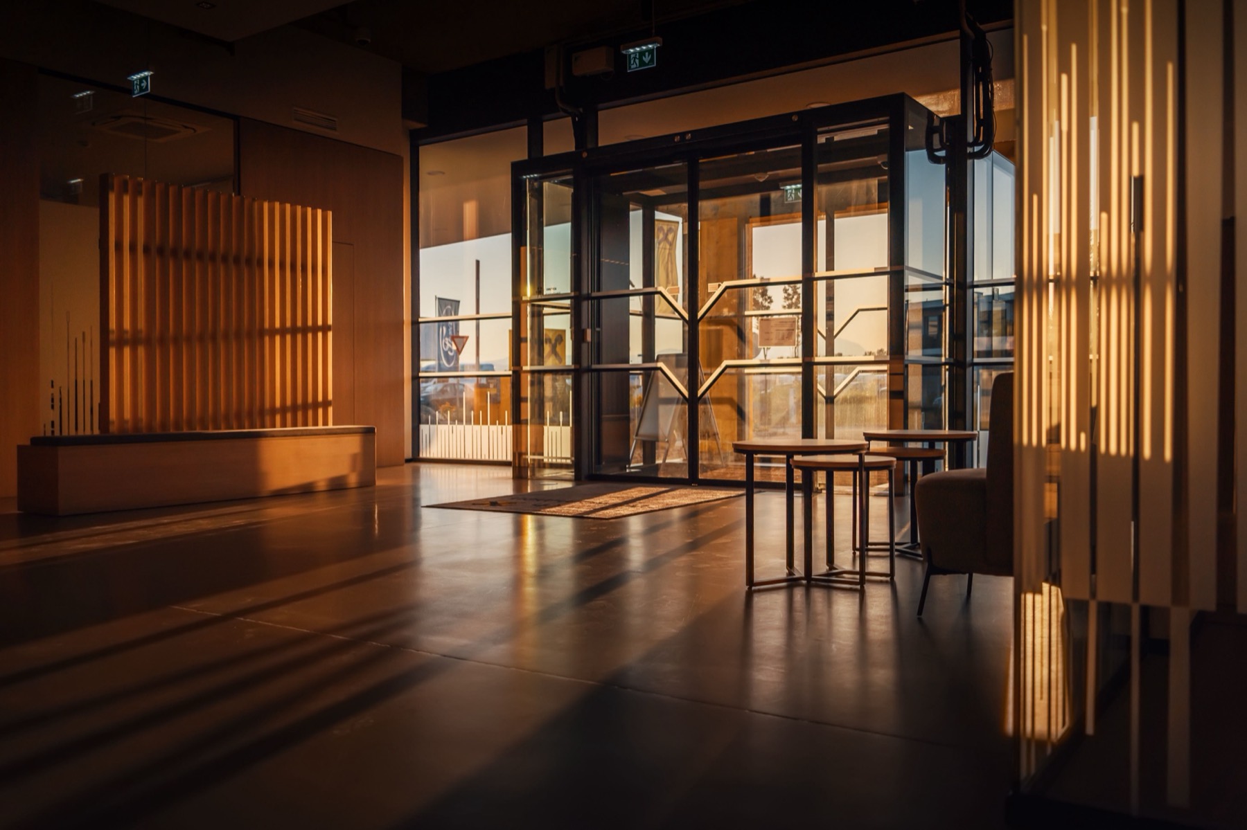 Sunlit hotel lobby with a vertical wood-slat screen, glass double doors and a polished floor at golden hour