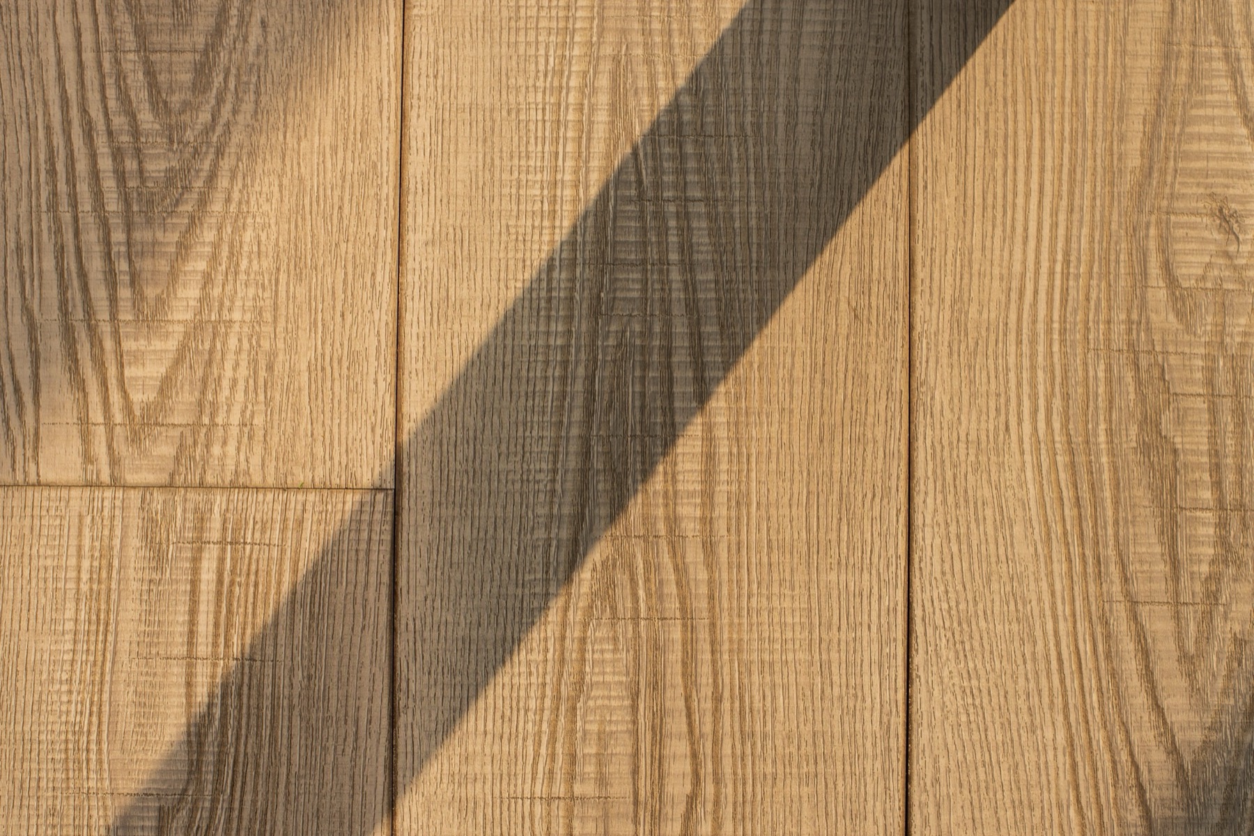 Close-up of pale oak wood panelling with a soft diagonal shadow falling across the grain